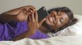 Beautiful and happy black Afro American woman lying relaxed on bed using internet mobile phone smiling cheerful networking social Royalty Free Stock Photo