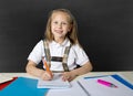 Beautiful happy blond junior schoolgirl smiling while doing school homework writing on notepad with pen Royalty Free Stock Photo