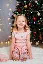 beautiful, happy blonde kid girl in pink dresses at the Christmas tree.