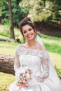 Beautiful happy bride with bouquet of flowers in park