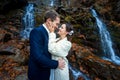 Beautiful happy bride softly touches face of her groom. Waterfall on background. Autumn in mountains Royalty Free Stock Photo