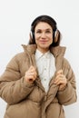 a beautiful happy brunette listens to music in brown headphones standing in a warm winter stylish jacket and smiles