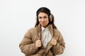 a beautiful happy brunette listens to music in brown headphones standing in a warm winter stylish jacket and smiles