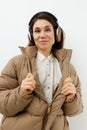 a beautiful happy brunette listens to music in brown headphones standing in a warm winter stylish jacket and smiles