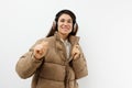 a beautiful happy brunette listens to music in brown headphones standing in a warm winter stylish jacket and smiles