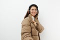 beautiful, happy, brunette listens to music in brown headphones, standing in a warm winter, stylish jacket and smiling