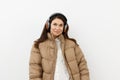 beautiful, happy, brunette listens to music in brown headphones, standing in a warm winter, stylish jacket and smiling