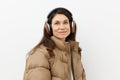 beautiful, happy, brunette listens to music in brown headphones, standing in a warm winter, stylish jacket and smiling