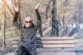 Beautiful happy caucasian  woman in jacket , hat and sunglasses enjoy  sitting on bench at city park or forest on sunny autumn day Royalty Free Stock Photo