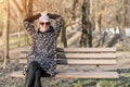 Beautiful happy caucasian  woman in jacket , hat and sunglasses enjoy  sitting on bench at city park or forest on sunny autumn day Royalty Free Stock Photo