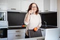 Beautiful happy modern charming elderly woman in glasses in the kitchen with a glass of water and an orange in her hands, the Royalty Free Stock Photo