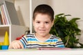 A beautiful happy child of 4 years old learns to read, sits in front of a book, looks into the camera and smiles