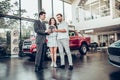 Beautiful happy couple buying a car at car salon showroom handsome car salesman showing something on a digital tablet to his Royalty Free Stock Photo