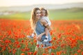 Beautiful smiling baby girl with mother are having fun in field of red poppy flowers over sunset lights, spring time Royalty Free Stock Photo