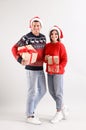 Beautiful happy couple in Santa hats holding Christmas gifts on light background Royalty Free Stock Photo