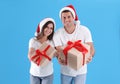 Beautiful happy couple in Santa hats holding Christmas gifts on light blue background Royalty Free Stock Photo