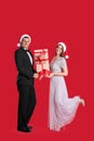 Beautiful happy couple in Santa hats holding Christmas gifts on red background Royalty Free Stock Photo