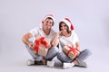 Beautiful happy couple in Santa hats sitting with Christmas gifts on light background Royalty Free Stock Photo