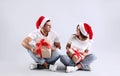 Beautiful happy couple in Santa hats sitting with Christmas gifts on light background Royalty Free Stock Photo