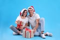 Beautiful happy couple in Santa hats sitting with Christmas gifts on light blue background Royalty Free Stock Photo