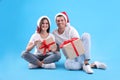 Beautiful happy couple in Santa hats sitting with Christmas gifts on light blue background Royalty Free Stock Photo