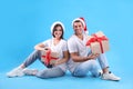 Beautiful happy couple in Santa hats sitting with Christmas gifts on light blue background Royalty Free Stock Photo