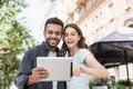 Beautiful happy couple using digital tablet. Joyful smiling woman and man looking at gadget in city street in summer