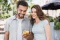 Beautiful happy couple using mobile phone in a city. Young joyful smiling woman and man looking at smartphone. Royalty Free Stock Photo