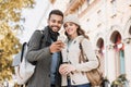 Beautiful happy couple using smartphone. Young joyful smiling woman and man looking at mobile phone in a city in autumn. Technolo