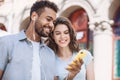 Beautiful happy couple using smartphone. Young joyful smiling woman and man looking at mobile phone in a city. Technology, travel