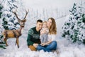 Happy family of young parents and a baby in winter sweaters in a fake winter forest, in the photo zone in the Studio. They are smi Royalty Free Stock Photo