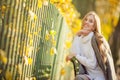 Beautiful happy girl with light brown hair is sitting on a bench near the fence in the autumn park Royalty Free Stock Photo
