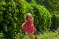 Beautiful happy girl in a red polka dot dress smiling on wild grape background. Cute joyful child with long blonde hair