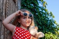 Beautiful happy girl in a red polka dot dress with soft toy smiling on wooden balcony. Cute joyful child with long hair Royalty Free Stock Photo