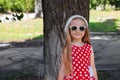 Beautiful happy girl in a red polka dot dress smiling on green leaves background.Cute joyful child with long blonde hair