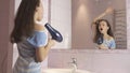 Beautiful happy girl teenager dries hair with hair dryer and sings and dances in front of a mirror in the bathroom