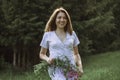 A beautiful happy girl in a white dress holds a bouquet of wild flowers in her hands. Portrait of a slender girl with a bouquet of