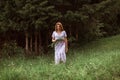 A beautiful happy girl in a white dress holds a bouquet of wild flowers in her hands. Portrait of a slender girl with a bouquet of