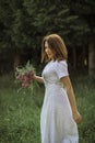 A beautiful happy girl in a white dress holds a bouquet of wild flowers in her hands. Portrait of a slender girl with a bouquet of