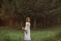 A beautiful happy girl in a white dress holds out a bouquet of wild flowers to the camera and smiles. Portrait of a slender girl