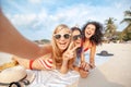 Beautiful happy girlfriends having fun on the beach taking selfies during vacation and travel