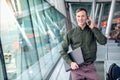 A beautiful happy guy with a laptop and shirt talking on the phone and smiling behind the window at the airport Royalty Free Stock Photo