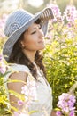 Beautiful, happy, healthy, sensual, sexy, young Asian woman enjoying summer sunlight in a flower garden. She is wearing a sun hat