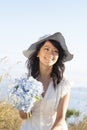 Beautiful, happy, healthy, smiling, young Asian woman holding fresh flowers outdoors in summer. She is wearing a feminine dress Royalty Free Stock Photo