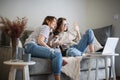 Beautiful happy lesbian couple sitting on sofa at home with pet dog bassengi online chatting using laptop, happy family Royalty Free Stock Photo
