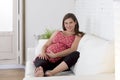 Beautiful happy 8 or 9 months pregnant woman lying relaxed on living room couch holding big belly Royalty Free Stock Photo