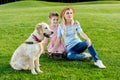 beautiful happy mother and daughter with golden retriever dog resting on green meadow Royalty Free Stock Photo