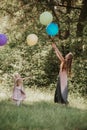 Beautiful happy mother with two daughters are having fun in green park and holding colorful balloons on summer sunny day. happy Royalty Free Stock Photo