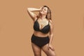 Beautiful and happy plus size woman in black underwear keeping eyes closed and smiling while standing in studio against