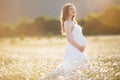 Beautiful happy pregnant girl on the field of daisy flowers in sunset lights